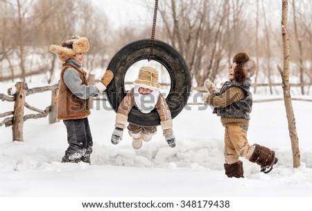 Three young children playing and swinging on the wheel, hanging in the backyard of the house, a warm winter day