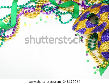 Carnival and Mardi Gras items including harlequin mask, green, gold and purple beads and ribbons and confetti on a warm white background. Copy space for your message. Horizontal composition