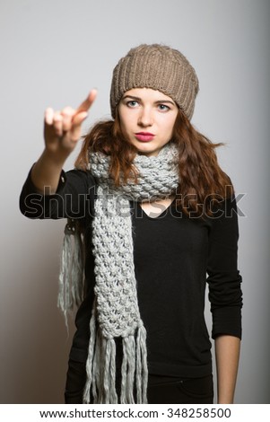 Bright girl presses a finger on the touch screen monitor, dressed in winter clothing, Christmas and New Year concept, studio photo isolated on a gray background