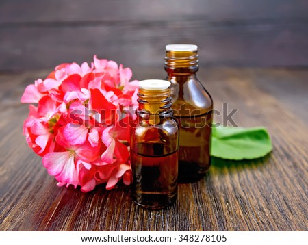Two bottle of oil with green leaf and flower of pink geranium on a wooden boards background Royalty-Free Stock Photo #348278105