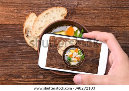 Hands taking photo soup with chicken and vegetables with smartphone.