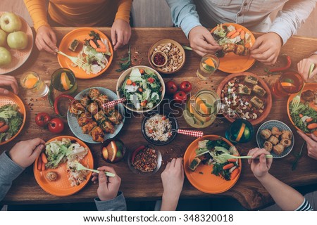 Enjoying dinner with friends. Top view of group of people having dinner together while sitting at the rustic wooden table Royalty-Free Stock Photo #348320018
