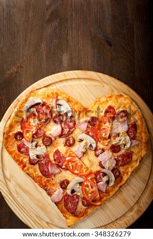 Pizza heart shape on dark wooden background top view. Thin pastry crust on wooden desk