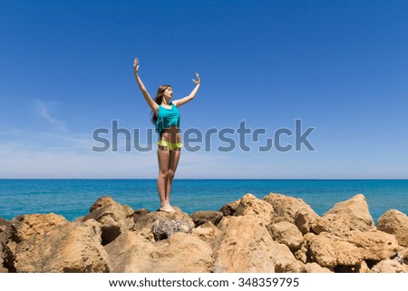 Long haired cheerful teenage brunette in beachwear, enjoys summer by the ocean.