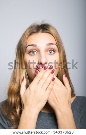 blonde girl laughs and covers her mouth with her hands, did not want to speak with clean skin, lifestyle concept studio photo isolated on a gray background