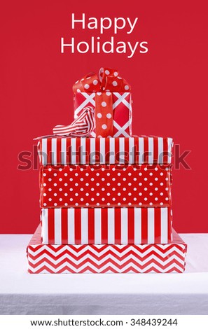 Stylish stack of festive Christmas red and white gifts on white table against a bright red background. 