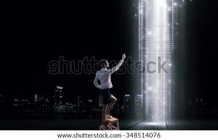 Back view of businesswoman standing on chair and reaching icon on virtual screen