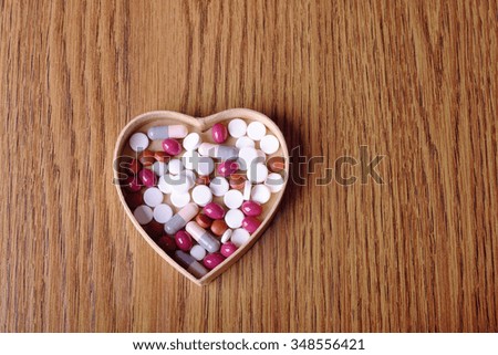 Pills in cardboard heart shape on wooden background