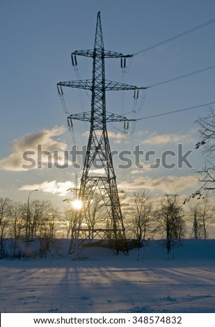 Electricity transmission lines are associated to  winter landscape. Industrial construction  silhouette against sunset background.