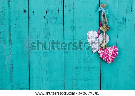 Brass house key with LOVE and pink rope country heart and tin heart hanging on antique teal blue old wood door; Valentines Day, real estate and home concept background with wooden painted copy space