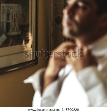 Handsome confident emotional exotic groom preparing putting on shirt closeup