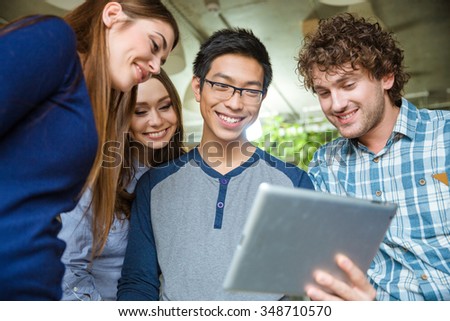 Joyful smiling young friends holding and using tablet