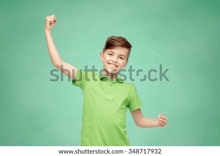 childhood, power, strength and people concept - happy smiling boy in green polo t-shirt showing strong fists over green school chalk board background