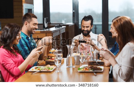leisure, technology, lifestyle and people concept - happy friends with smartphones taking picture of food at restaurant
