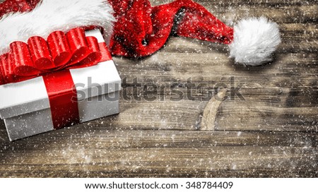 Christmas decoration. Gift box with red ribbon bow on wooden background. Vintage style toned picture with falling snow effect