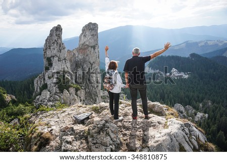 Color picture of an elderly couple holding hands and waving on top of a mountain