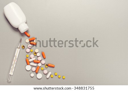 Pills and capsules spilling out of bottle with thermometer closeup on a gray background. Top view. Copy space. Medicine concept