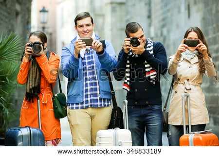 Group of smiling young tourists walking through street with camera and smartphone