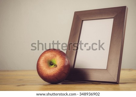Still life with apple and white photo frame on wooden table over grunge background.