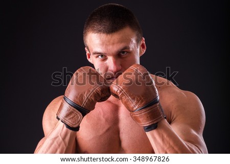 Muscular man in boxing gloves on a dark background. Professional boxer boxing shows muscle in racks. Beautiful muscular body boxer. Photos for sporting magazines, posters and websites.