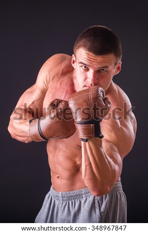Muscular man in boxing gloves on a dark background. Professional boxer boxing shows muscle in racks. Beautiful muscular body boxer. Photos for sporting magazines, posters and websites.