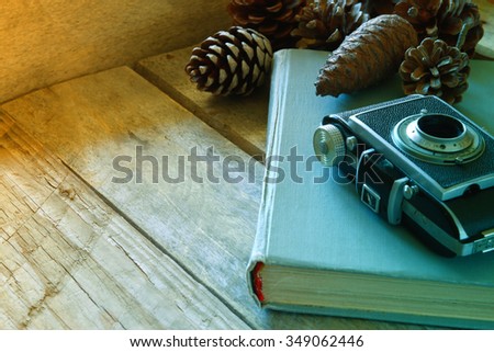 old book, vintage photo camera next to pine cones on wooden table. selective focus
