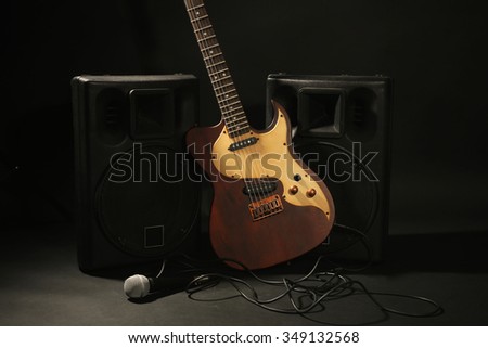Big loudspeakers with electric guitar and microphone on black background