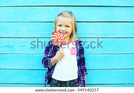 Happy smiling child with sweet caramel lollipop having fun over colorful blue background