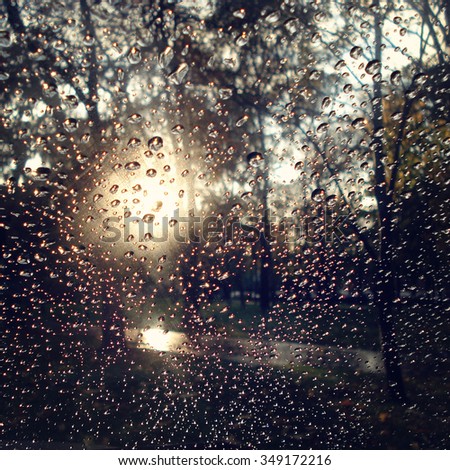 Autumn park through car glass. Retro filter. Drops of rain on the car window. Aged photo. Glare from the sun through wet window glass. Rainy day in the city.