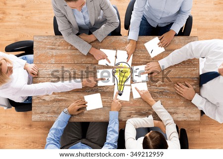 business, office people, startup and teamwork concept - close up of creative team sitting at table and putting together puzzle pieces with light bulb picture Royalty-Free Stock Photo #349212959