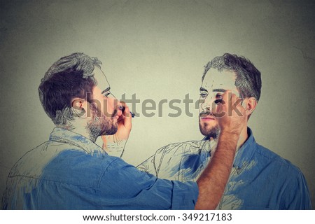 Create yourself concept. Good looking young man drawing a picture, sketch of himself on grey wall background. Human face expressions, creativity Royalty-Free Stock Photo #349217183