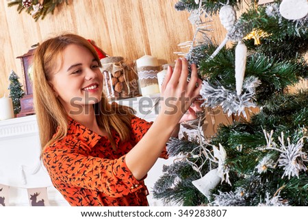 Cute girl in red dress happily decorating a Christmas tree