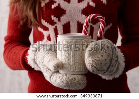 Woman hands in cute christmas mittens holding a cup of coffee or cocoa with a candy cane