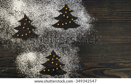 On a brown wooden desk background scattering of flour and powdered sugar in the form of Christmas trees before the new year, there is an empty space for your text or picture