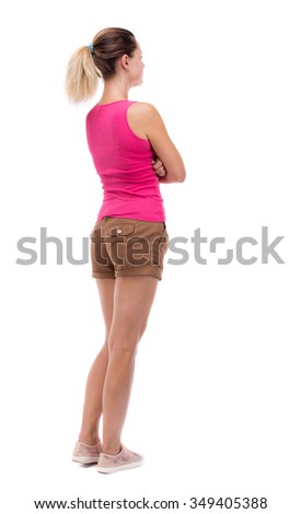 back view of standing young beautiful  woman.  girl  watching. Rear view people collection.  backside view person.  Isolated over white background. Blonde in brown shorts stands with his arms folded