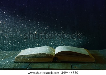 abstract image of open antique book on wooden table. selective focus. retro filtered and toned with glitter overlay