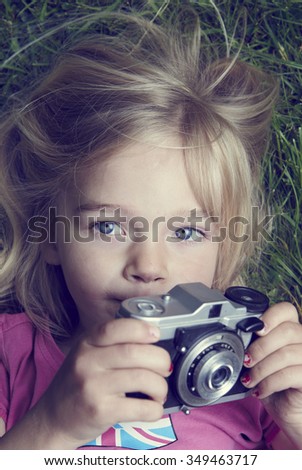 Portrait of little girl taking picture using vintage old retro film camera, lying on grass background