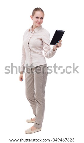front view of standing young beautiful  girl with tablet computer in the hands of. girl  watching.  Isolated over white background. A girl in a white jacket smiling read e-books.