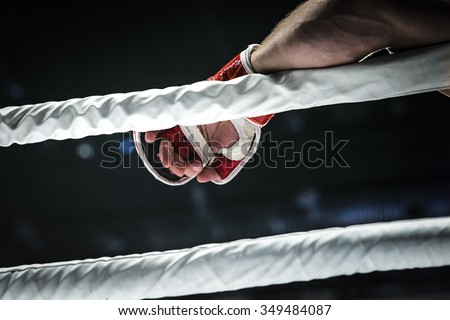 closeup hand of fighter MMA in glove lays ropes of ring