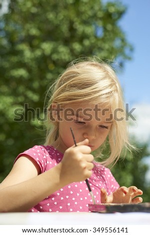 A girl painting with water colors (watercolors), painting a paper plate with watercolor paints outside in garden