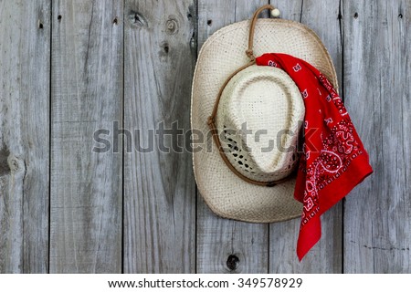 Cowboy hat with red bandanna hanging on antique rustic wooden background