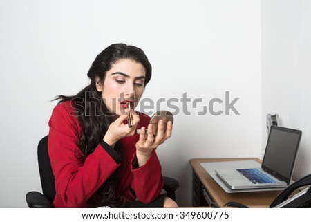 Young pretty business woman in the office taking notes looking bored. She is wearing a black blouse and a red Jacket
