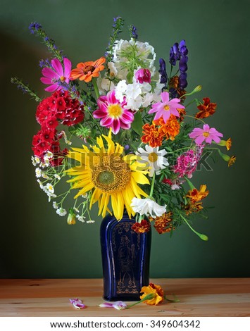 Still life with a bouquet of country flowers in a blue vase on a green background.