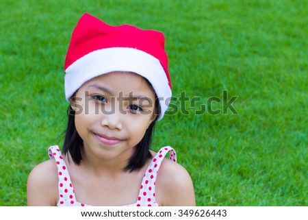 Cute girl child wearing red christmas hat on green Lawn