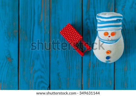Red sled and handmade snowman on blue wooden background. Xmas card with empty space for text. Unique perspective, top view.