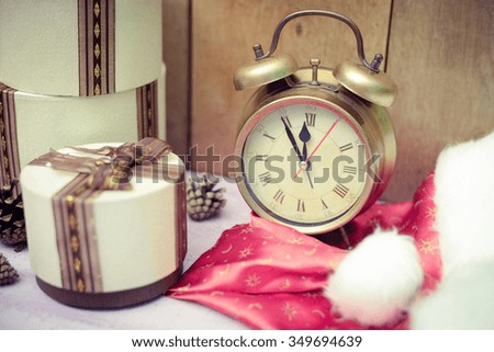 Picture of three round gift boxes with retro alarm clock. Santa hat and presents on plank table indoor background.