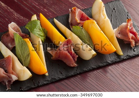 Appetizer of Parma ham and vegetables on wooden panel, selective focus