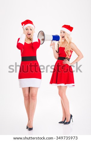 Attractive amusing sisters twins in santa claus costumes and hat speaking in loudspeaker over white background