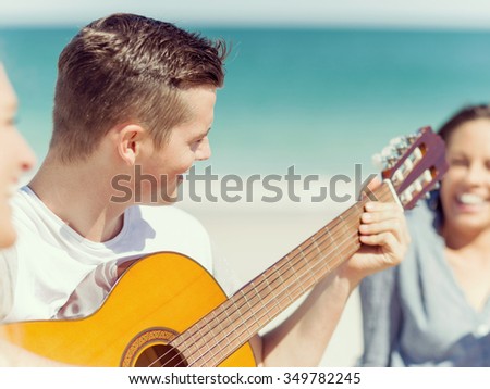 Picture of young smiling man playing guitar on beach