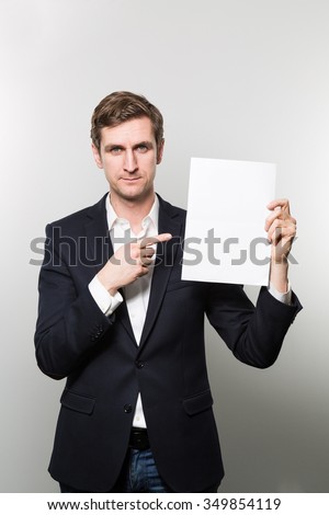 Blond-haired european businessman shows something on a piece of paper and looks exhausted into the camera while in front of a gradient background